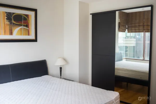 Condominium for rent or sale in Khlong Toei, Bangkok - Bright bedroom with double bed, artwork and a mirrored sliding wardrobe.
