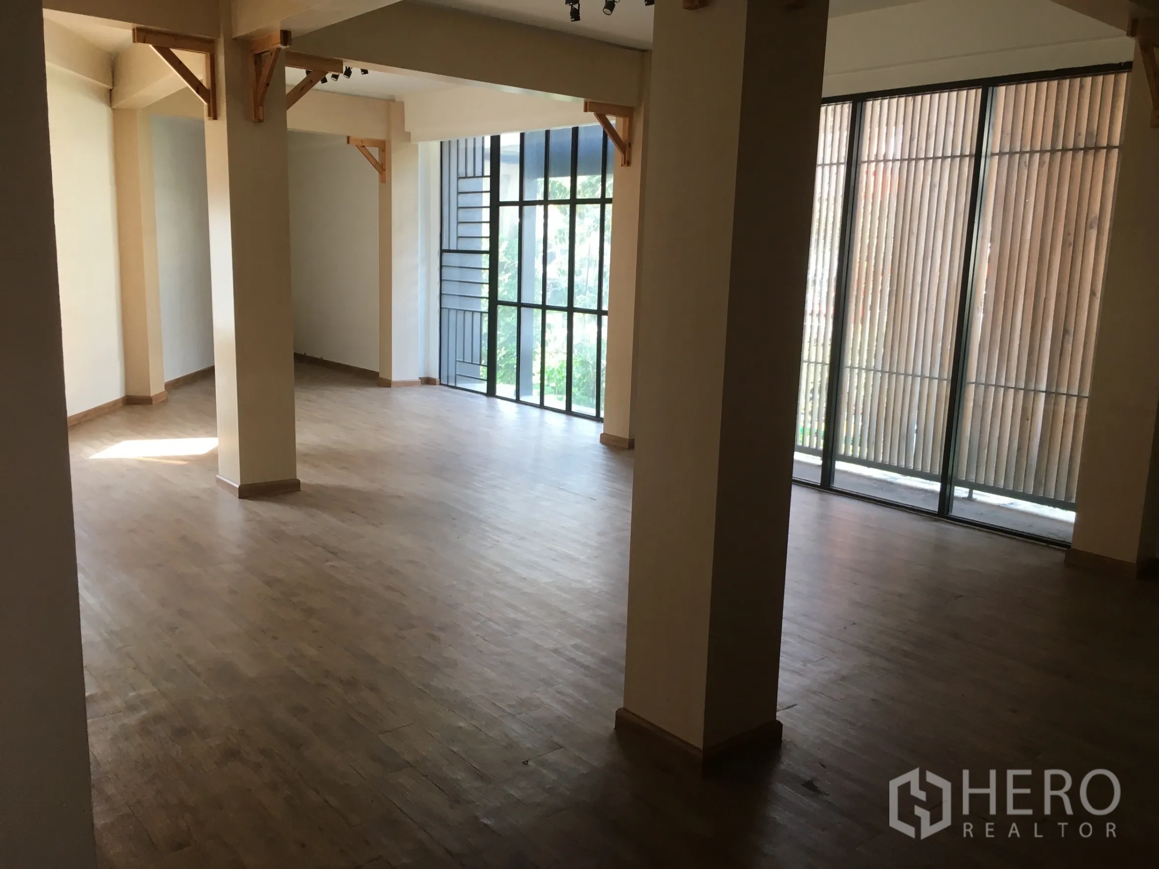 零售空间 出租在Khlong Toei, Bangkok - 明亮展厅，木地板、立柱与落地窗，配垂直格栅。