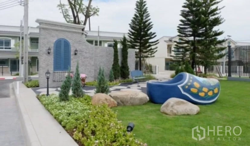 Townhouse for rent in Bang Phli, Samut Prakan - Gated community entrance with landscaped garden, pines and seating.