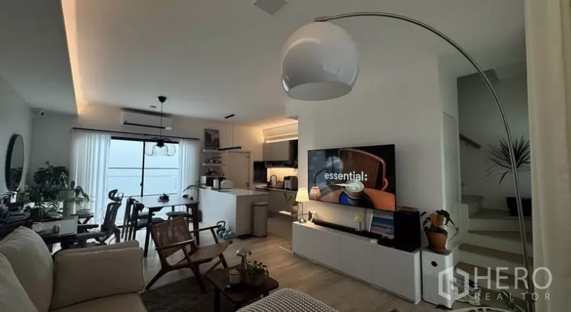 Townhouse for rent in Bang Phli, Samut Prakan - Contemporary living room with arc floor lamp, media console, staircase and kitchen in the background.