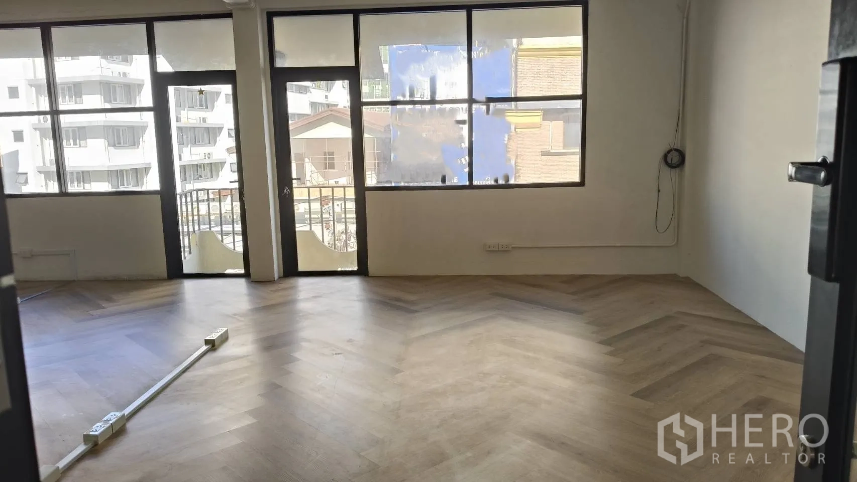 Retail Space for rent in Watthana, Bangkok - Bright open retail room with large windows, a glass door to a small balcony, and herringbone wood floors.