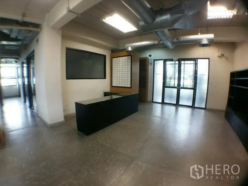 办公空间 出租在Phra Khanong, Bangkok - 接待区设前台柜台、磨砂玻璃门与工业风管道天花。