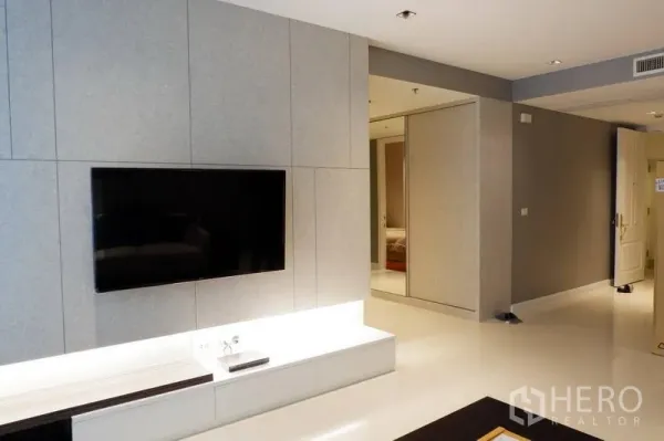 Condominium for rent in Pathum Wan, Bangkok - Modern media wall with mounted TV and lighted console leading to a hallway with mirrored closet.