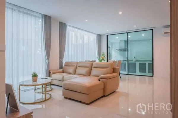 Detached House for rent in Bang Phli, Samut Prakan - Bright living room with large beige sectional sofa, sheer curtains and sliding glass doors to the kitchen.