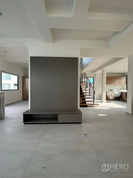 บ้าน ให้เช่าในWatthana, Bangkok - ห้องนั่งเล่นกว้าง ผนังวางทีวี เพดานหลุม และบันไดเชื่อมต่อไปยังครัว