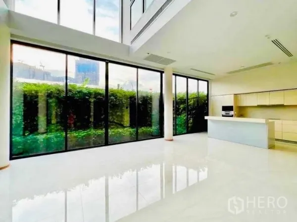 บ้าน ขายในHuai Khwang, Bangkok - ห้องนั่งเล่นเพดานสูงโปร่ง ผนังกระจกเต็มบาน พร้อมครัวไอส์แลนด์ มองเห็นสวนแนวรั้ว