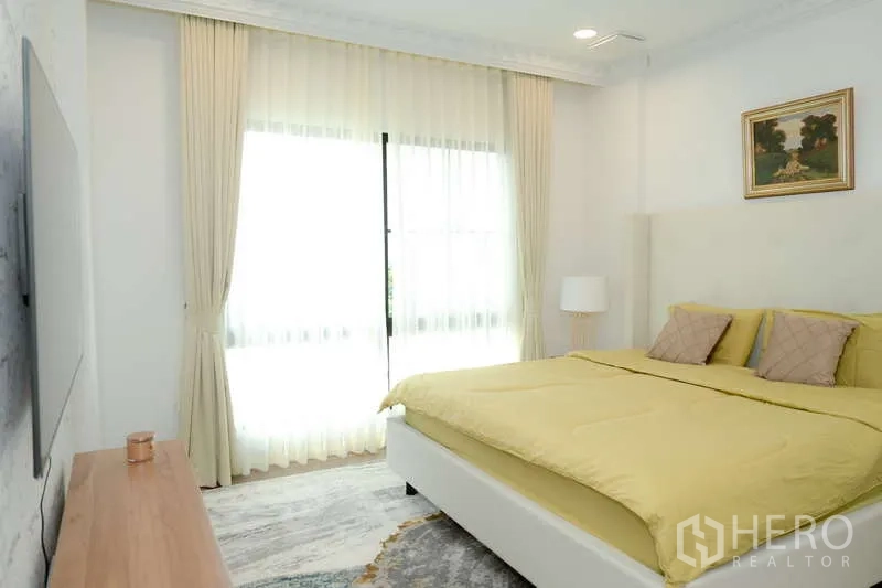 บ้าน ให้เช่าหรือขายในSaphan Sung, Bangkok - ห้องนอนพร้อมประตูกระจกบานเลื่อนออกระเบียง ผ้าม่านโปร่ง และผนังทีวี