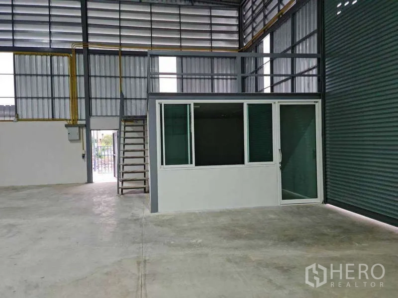 货栈 出租在Bang Bua Thong, Nonthaburi - 内部设有玻璃办公室与夹层平台，旁为高卷闸门。