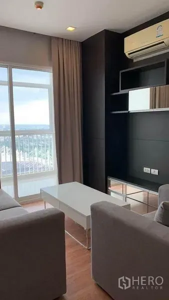 公寓 出租或出售在Bang Na, Bangkok - 明亮客厅配灰色沙发、白色茶几、内置电视墙与带城市景观的阳台。