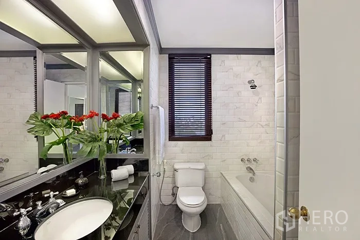 Condominium for rent in Khlong San, Bangkok - Bathroom with bathtub, black stone countertop, mirrored cabinets and a window with blinds.