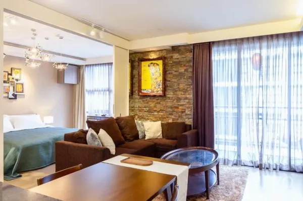 公寓 出租在Watthana, Bangkok - 明亮客厅，转角沙发与石纹特色墙，轻薄窗帘，卧室以推拉隔断相连。