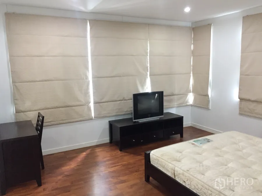 公寓 出租在Khlong Toei, Bangkok - 明亮卧室，木地板，书桌与电视柜，大窗配米色百叶帘。