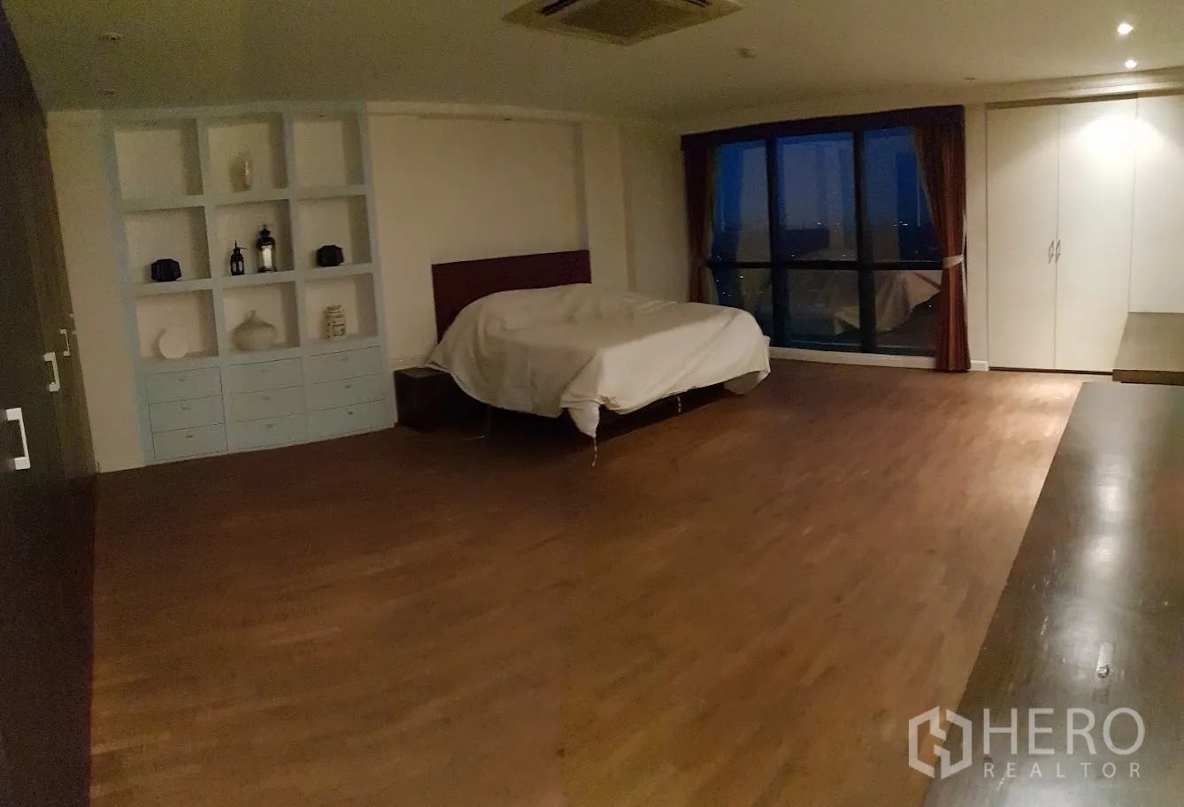 Condominium for rent in Yan Nawa, Bangkok - Extra‑large bedroom with wood flooring, built‑in shelving and nighttime city views.