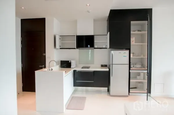 Condominium for rent in Watthana, Bangkok - Open-plan kitchen with island sink, two-tone cabinets, refrigerator, microwave, and ample pantry storage.