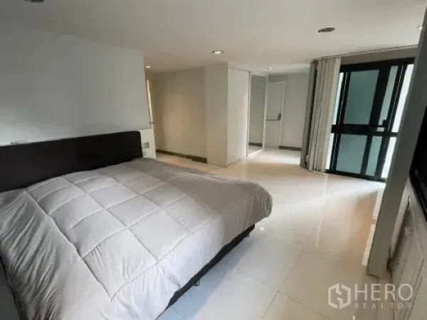 Condominium for rent - Spacious bedroom with large bed, light tile flooring, built-in storage, and sliding glass door to a balcony.