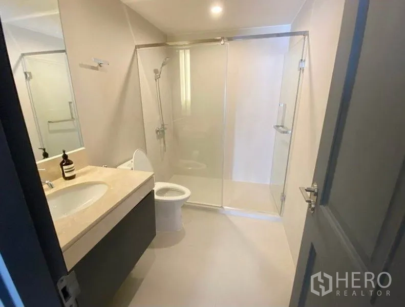 Condominium for rent in Pathum Wan, Bangkok - Contemporary bathroom with wide vanity, glass-enclosed shower and toilet.
