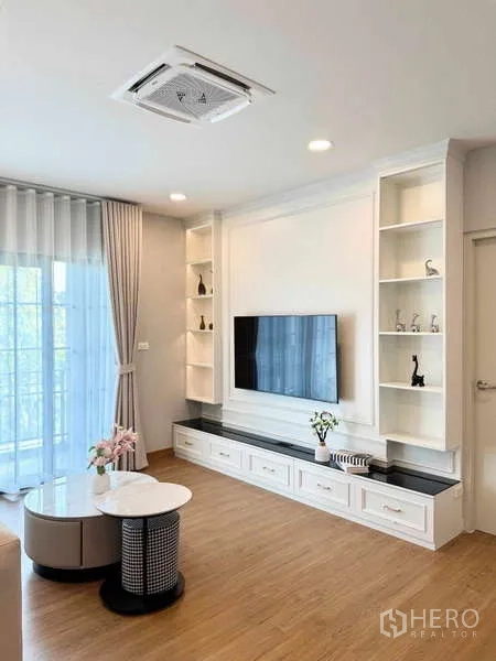 Detached House for rent or sale in Bang Phli, Samut Prakan - Family room with TV wall, open shelves, wood floors, sliding glass doors and cassette ceiling AC.