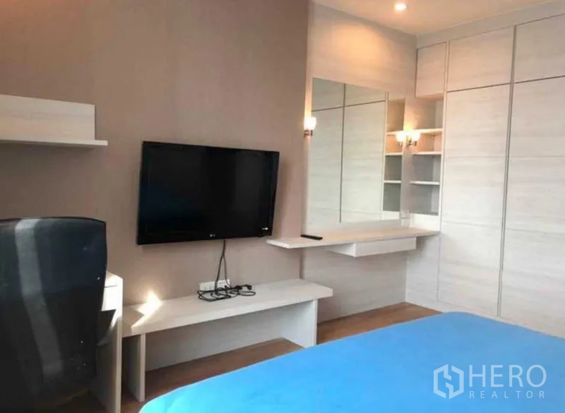 Condominium for sale in Khlong Toei, Bangkok - Bedroom workspace with wall-mounted TV, built-in wardrobe and vanity mirror.