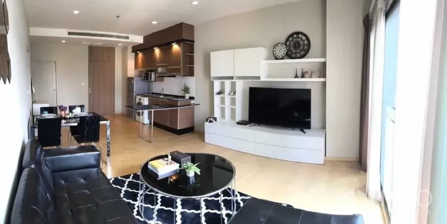 Condominium for rent in Watthana, Bangkok - Open-plan living area showing sofa, TV cabinet, and contemporary kitchen.