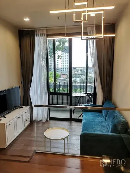 คอนโด ให้เช่าในRatchathewi, Bangkok - ห้องนั่งเล่นอบอุ่น โซฟาสีเขียวอมฟ้า โคมไฟดีไซน์ ตู้วางทีวี และระเบียงชมวิวเมือง ใกล้อนุสาวรีย์ชัยฯ