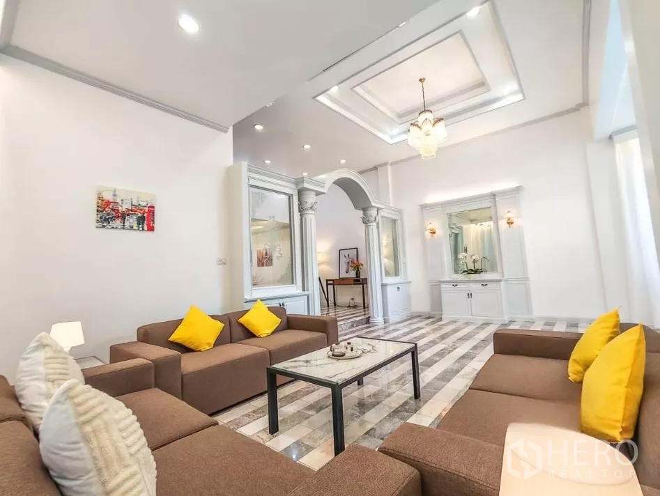 บ้าน ให้เช่าในYan Nawa, Bangkok - ห้องนั่งเล่นสไตล์คลาสสิก มีเสาโคโลเนียล เพดานหลุม และโซฟาสีน้ำตาลพร้อมหมอนสีเหลือง