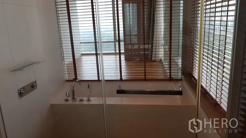 Condominium for rent in Pathum Wan, Bangkok - Deep soaking tub beside a glass partition with blinds facing the bedroom.