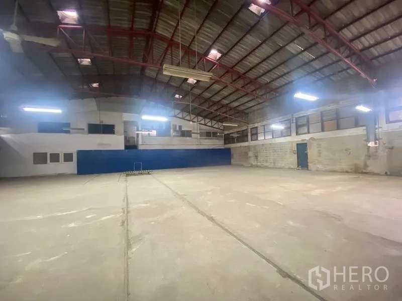 Warehouse for rent or sale in Suan Luang, Bangkok - Central hall of the warehouse featuring a clear-span concrete floor and a long blue partition wall beneath a corrugated roof.