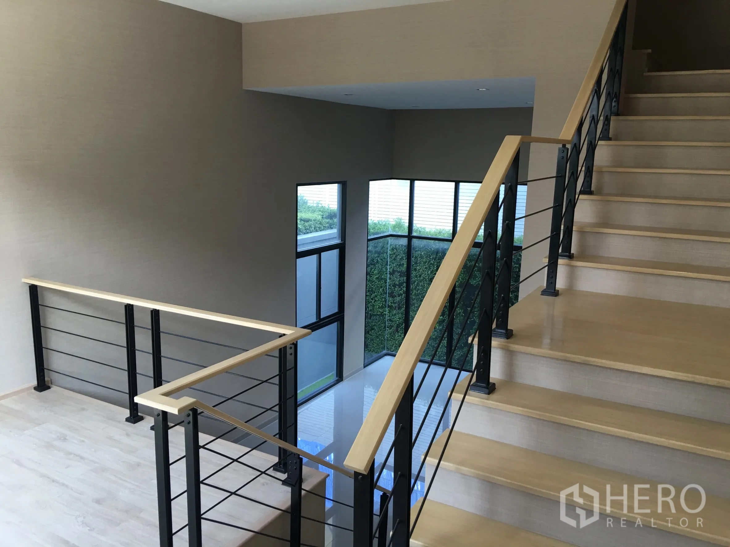 Townhouse for rent or sale in Suan Luang, Bangkok - Wood staircase with black metal railings and corner windows.