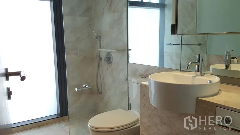 Condominium for rent in Sathon, Bangkok - Modern bathroom with glass shower, rain showerhead, marble vanity with vessel sink, large mirror, and frosted window.