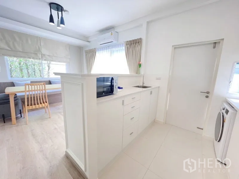 联排别墅 出租在Prawet, Bangkok - 厨房半岛带水槽与收纳，面向餐椅角与明亮窗户。