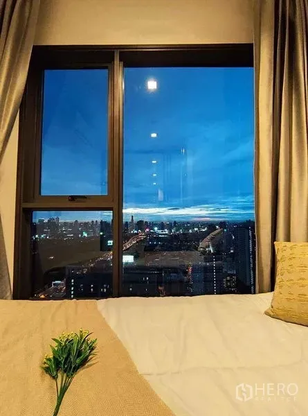公寓 出租在Ratchathewi, Bangkok - 卧室大窗俯瞰曼谷夜景，床与窗帘营造温馨氛围。