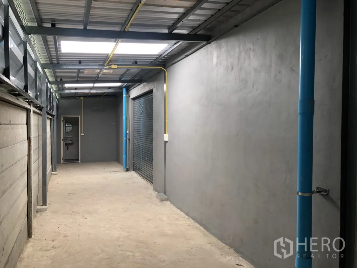 คลังสินค้า ให้เช่าในLam Luk Ka, Pathum Thani - ทางเดินบริการมุงหลังคา มีท่อประปาสีฟ้าและท่อไฟสีเหลือง เชื่อมไปยังห้องยูทิลิตี้
