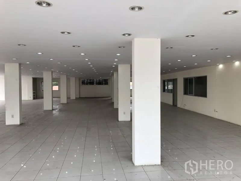 Retail Space for rent in Lam Luk Ka, Pathum Thani - Deep open‑plan space with tiled floors, structural columns and built‑in office windows along one wall.