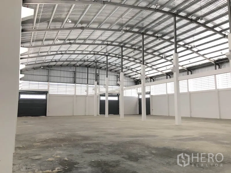 Warehouse for rent in Samut Prakan - Open storage hall with ventilation panels and multiple roller shutter access points.