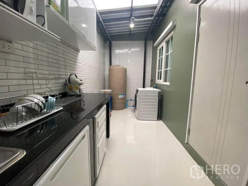 Townhouse for sale in Saphan Sung, Bangkok - Extended kitchen and utility area with ample counter space, washing machine and water tank under a skylight roof.