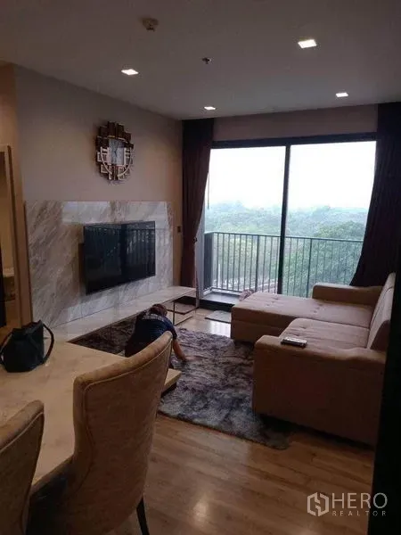 คอนโด ให้เช่าหรือขาย - ห้องนั่งเล่นสไตล์โมเดิร์น โซฟาเข้ามุม ผนังทีวีหินอ่อน พร้อมระเบียงวิวต้นไม้