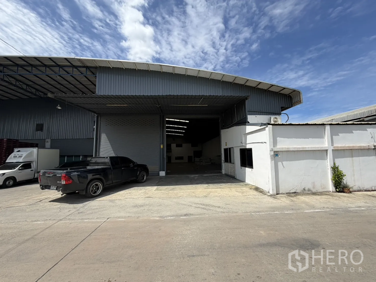仓库 for rent in Khlong Luang, Pathum Thani - 仓库外观设有宽卷闸门与有顶装卸区，前方为小型办公室和混凝土空地可停车。