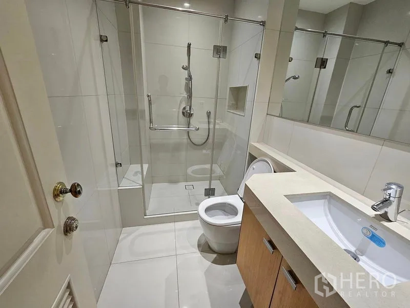Condominium for rent or sale in Pathum Wan, Bangkok - Modern bathroom with glass-enclosed shower, vanity and large wall mirror.