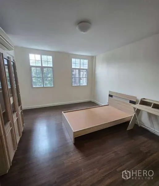 Townhouse for sale in Watthana, Bangkok - Bright bedroom with wood flooring, large windows and a minimalist bed frame.