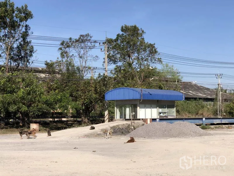Warehouse for rent in Phra Nakhon Si Ayutthaya - Entry checkpoint with small guardhouse and open yard beside trees and utility lines.