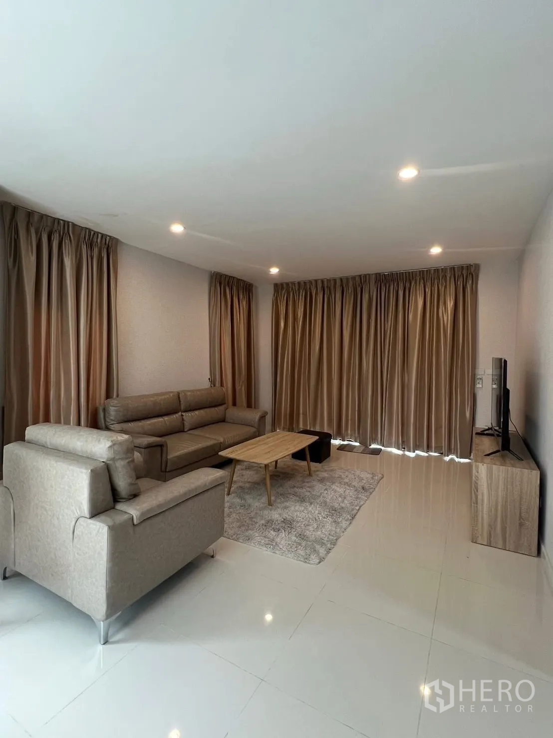 Detached House for rent in Bang Phli, Samut Prakan - Daytime living room with full-length curtains, gray sofa set, TV console and glossy tiles.