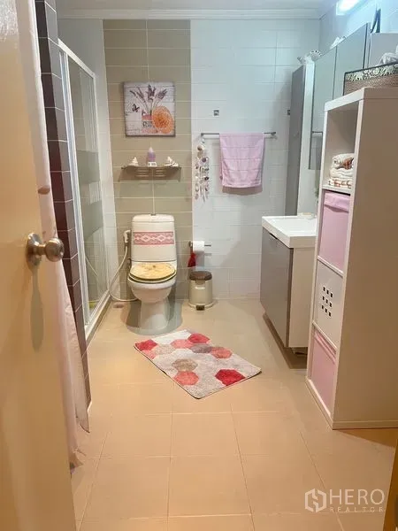 公寓 出售在Watthana, Bangkok - 宽敞浴室，带玻璃淋浴间、洗手台、置物架与淡粉色点缀的曼谷公寓。