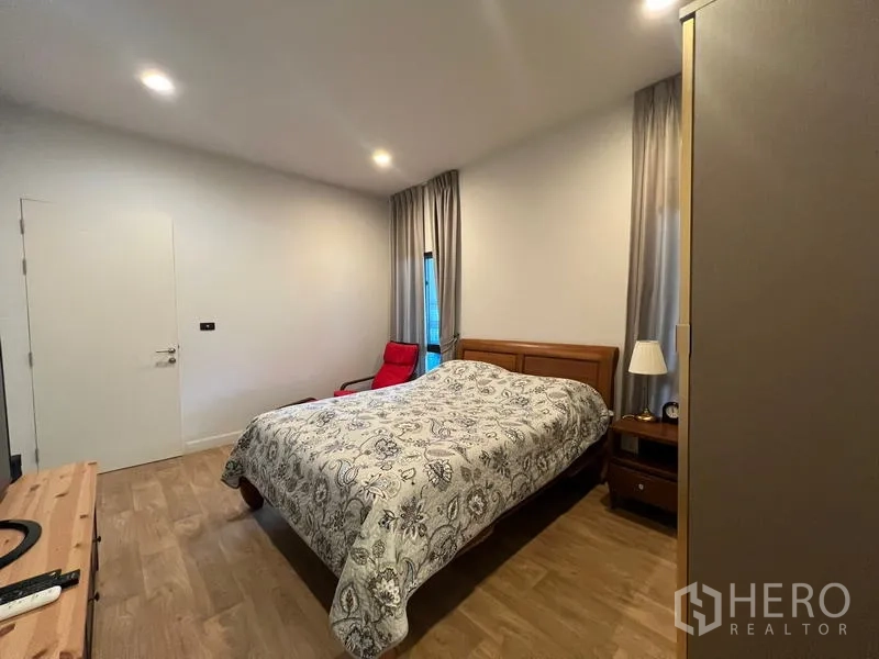 Detached House for rent in Bang Kapi, Bangkok - Cozy bedroom with wooden bed, bedside tables and a red lounge chair.
