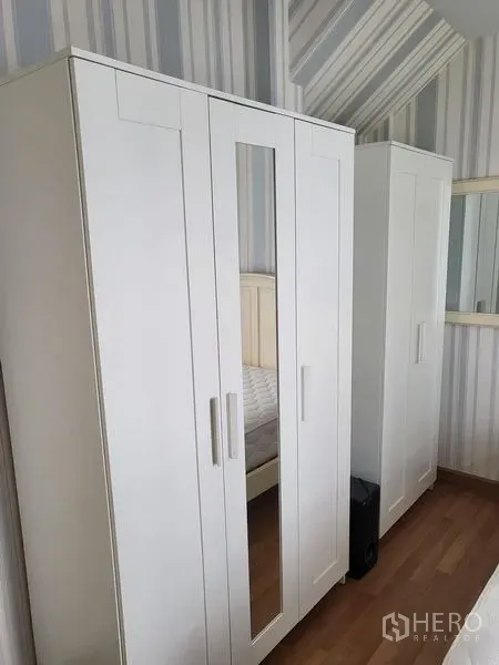 Townhouse for rent in Wang Thonglang, Bangkok - White wardrobes with mirror doors against striped wallpaper in a bedroom.