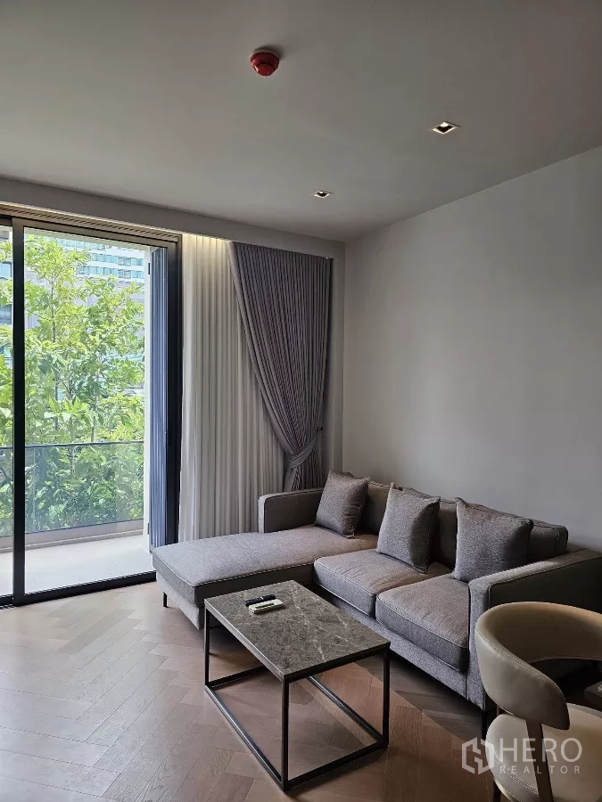 公寓 出租在Watthana, Bangkok - 转角沙发与大理石茶几，旁是落地窗，景观绿意盎然。