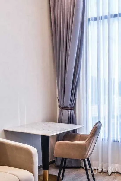 Condominium for rent in Huai Khwang, Bangkok - Cozy dining nook with marble-top table and upholstered chair by window.