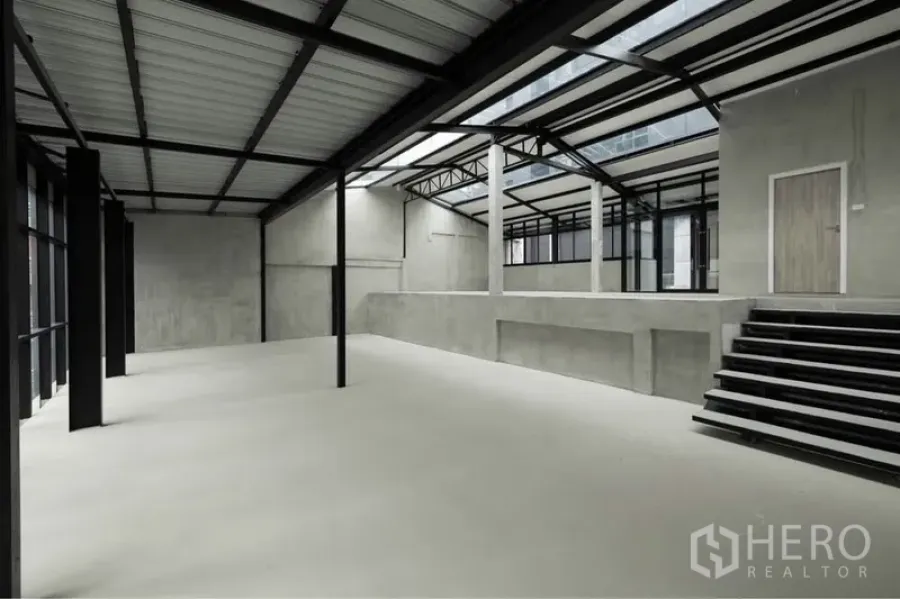 零售空间 出租在Watthana, Bangkok - 工业风零售大厅，带抬高平台、宽阶梯、外露桁架与采光天窗。