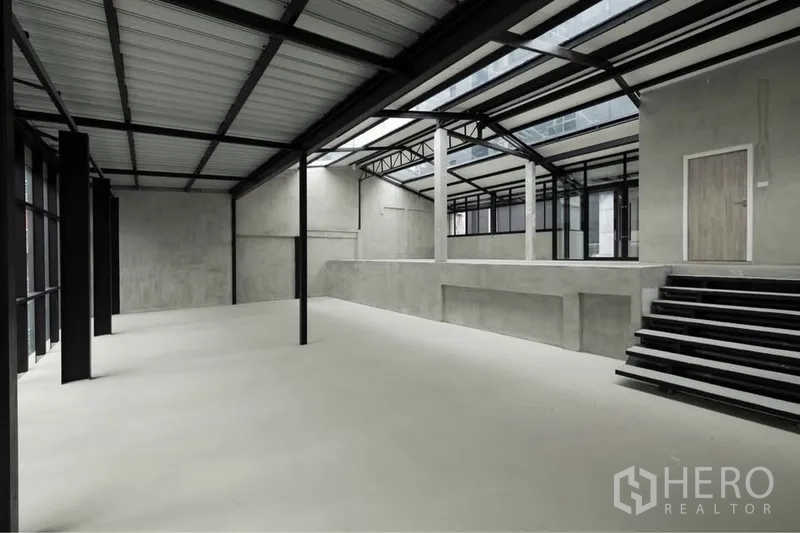 零售空间 出租在Watthana, Bangkok - 工业风零售大厅，带抬高平台、宽阶梯、外露桁架与采光天窗。