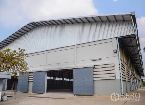 Factory for rent in Pathum Thani - High-gable warehouse exterior with wide sliding doors and a concrete loading apron.