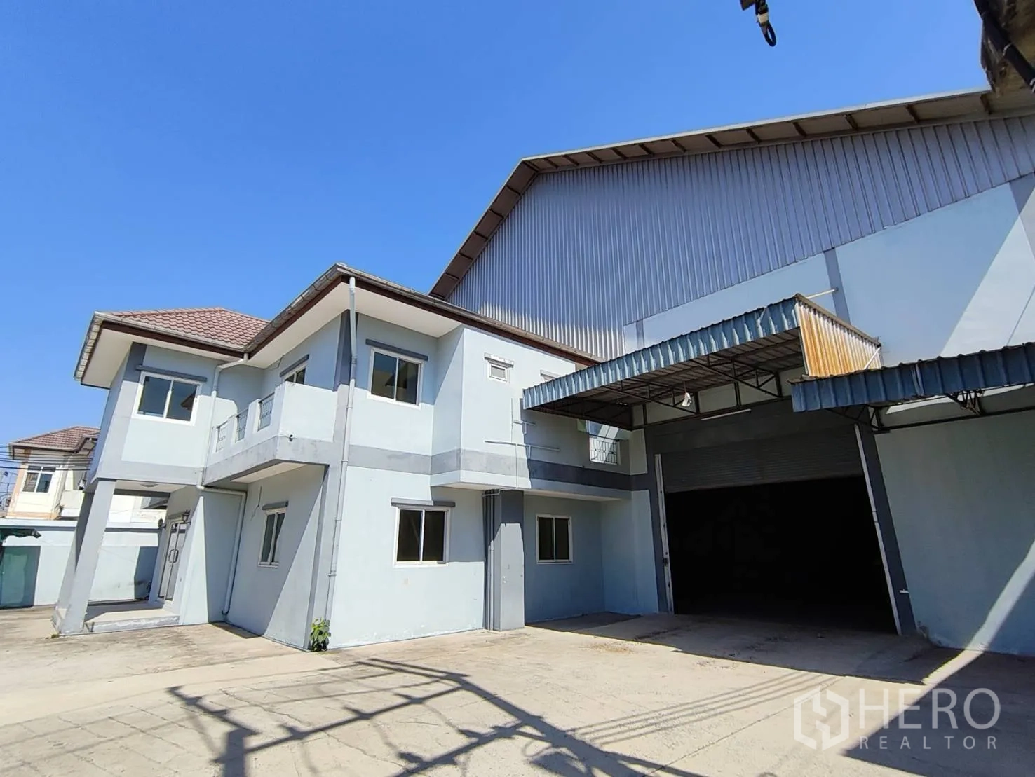 Factory for rent in Krathum Baen, Samut Sakhon - Front view of the factory showing the covered loading bay and roller shutter beside the two-storey house.